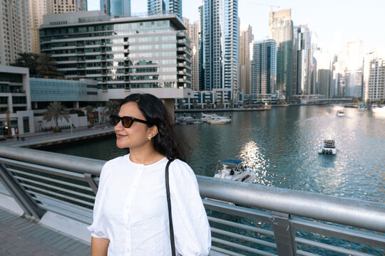 Woman enjoying Dubai Marina waterfront with modern skyline and yachts in creek, modern residential and hotel apartments in Dubai marina
