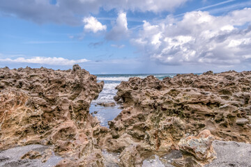 A rocky beach with a small opening in the rocks. The sky is blue and the water is calm