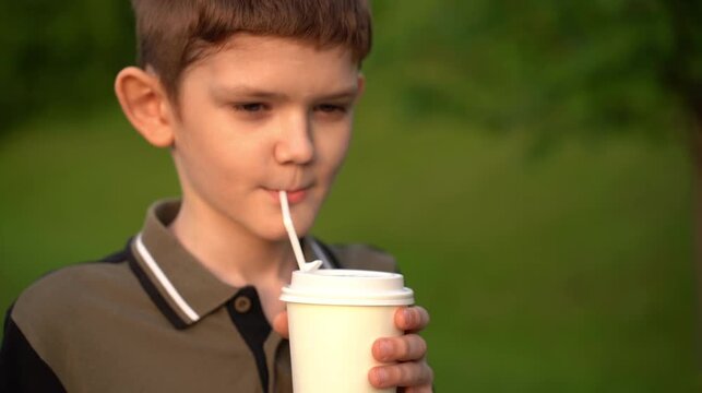 boy drinks coffee through a straw from a disposable paper cup.