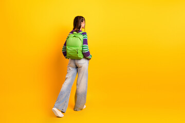 Young woman with green backpack walks on a bright yellow background wearing a striped sweater and casual jeans for a vivid fashion lifestyle