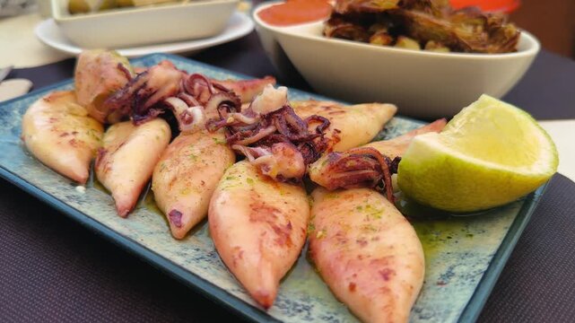 Baby squid in basil sauce with lemon sprinkles on a plate at a snack bar. High quality 4k footage