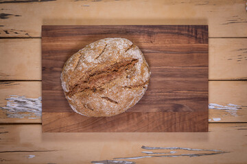 Rustic Homemade Bread On Rectangular Wooden Board Over Worn Beige Table
