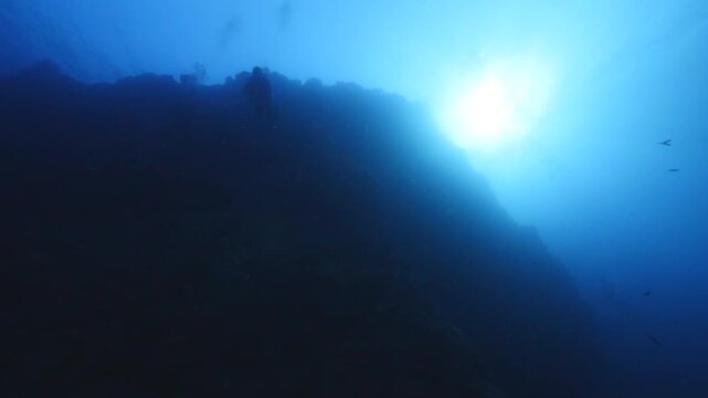 scuba divers descending from a hill underwater with sun beams and rays