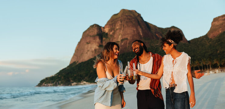 Three friends on a beach with drinks at sunset