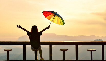 Silhouette of Woman sitting on chair hold colorful umbrella looking Foggy in the mountains with dramatic sky at sunrise. retro and vintage style