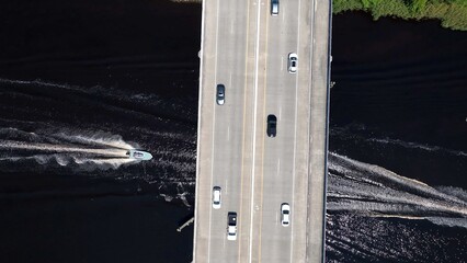 Drone view looking down on traffic traveling across Intracoastal waterway in Myrtle Beach, SC as boat motor underneath bridge