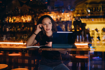 Fototapeta premium Freelancer woman working in bar with notebook, tablet and smartphone — embodying remote flexibility and full digital immersion in a modern multitasking setting.