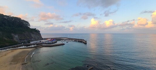 Aerial view of a coastal harbor and beach at sunset with golden clouds over the ocean