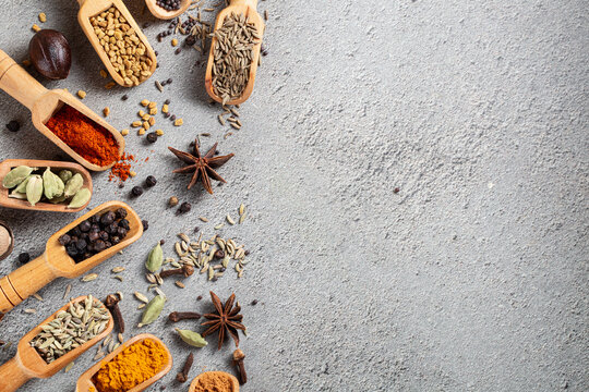 Assorted Indian spices in wooden scoops scattered on a textured gray surface with empty space for copy, showcasing vibrant colors and diverse textures