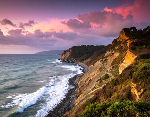 Coastal scene during a vibrant sunset. Rocky cliffs meet the turbulent sea as clouds are ablaze with pinks, purples, and oranges