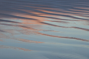 Evening sky reflection in shiny surface of rippling beach sand