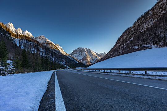 vista panoramica della strada che percorre la Valle Rio del Lago tra le montagne che portano al paese di Cave del Predil, nel Friuli nord-orientale, in Italia, al tramonto, in inverno