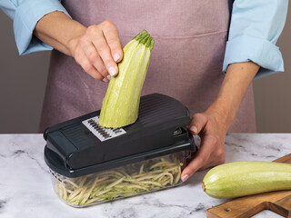 A woman slices zucchini with a vegetable cutter, authentic photograph, not AI-generated