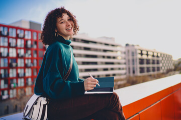 Freelancer looks over shoulder smiling, holding stylus and tablet on red wall, evoking confidence, freedom and ease of remote creative work powered by everyday mobile technology. © BullRun