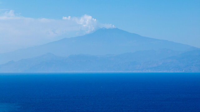 Silhouette of Mount Etna, located in Sicily, seen from Calabria. It is the highest volcano in Italy. In the foreground, the sea waters of the Strait of Messina. A plume of white smoke is visible.
