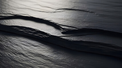 Close-up of layered dark grey slate texture with rough edges and dramatic light casting deep shadows, abstract natural background