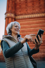 Fototapeta premium Woman checks her smartphone with concentrated expression while walking in city daylight — capturing focused engagement and personal tech use in everyday life.