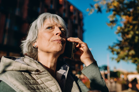 Happy older woman laughs while talking on smartphone outside, expressing joy and comfort in mobile communication &mdash; a vivid snapshot of tech‑enabled everyday life.