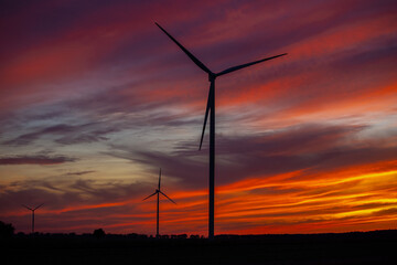 Obraz premium Silhouettes of wind turbines against a fiery sunset sky with dramatic clouds