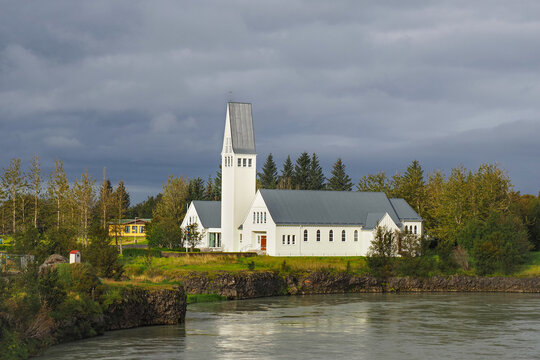Selfosskirkja, Lutheran church and convention center. Classically Nordic building in southern Iceland, Kirkjuvegur, Selfoss. Beautiful white Church with tower, built on cliff just around the riverbend