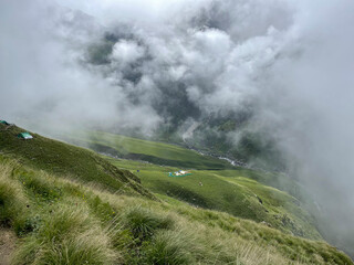Fototapeta premium Clouds cover green hills with a river winding below in a remote mountain area during daytime