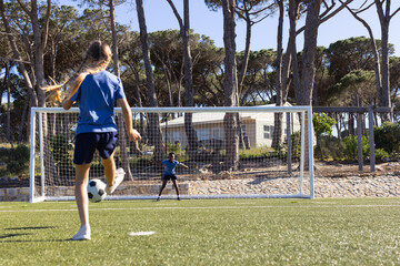 Youth teammates in blue tops kicking soccer ball toward full-size goal on turf, copy space