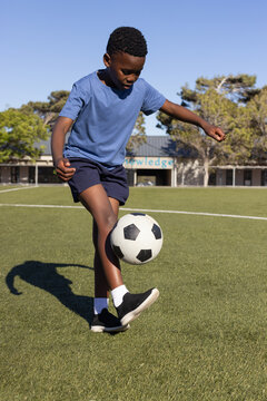 African male youth in blue tee shorts controlling black white soccer ball on school turf, balancing