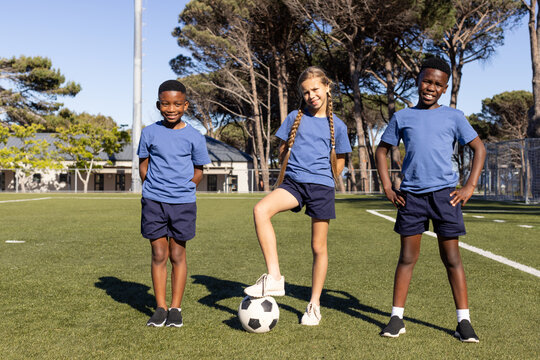 Diverse children posing on artificial-turf soccer field with soccer ball and matching blue shirts