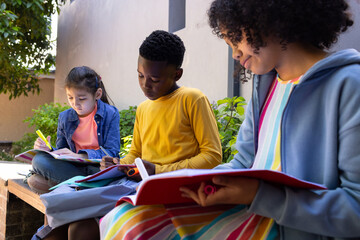 Diverse children sitting on low stone bench in courtyard with backpacks, marking and writing notes