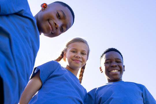 Diverse teenage friends leaning toward camera under clear blue sky, wearing blue shirts and braids