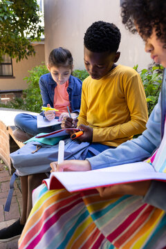 African American teens in bright clothes studying on brick ledge at courtyard notebooks backpack