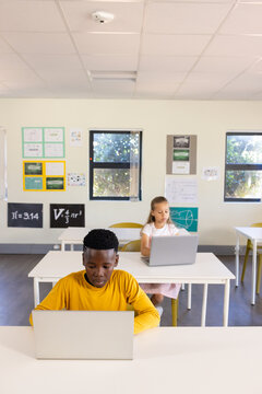 Classmates sitting at desks in classroom, male in yellow shirt using silver laptop, female working