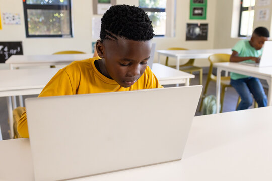 African American school-age boys working on laptops at classroom desks with yellow chairs