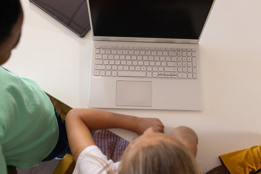 Silver laptop is sitting centered on white rectangular table, dark tablet and yellow cloth visible