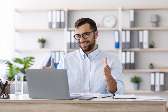 Happy mature caucasian guy with beard in glasses work at laptop, making video call and gesturing in office or living room interior. Businessman, teacher, tutor. Meeting during COVID-19 outbreak