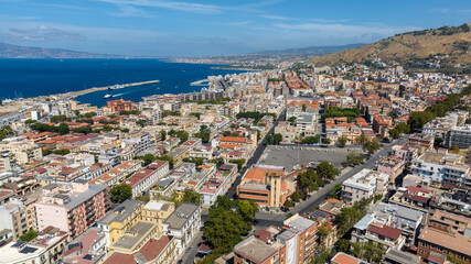 Obraz premium Aerial view of the outskirts of the city of Reggio Calabria, Italy. In the background is the city port, and beyond the Strait of Messina, Sicily can be seen, separated by the sea.