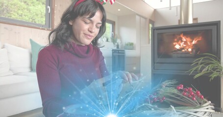 Naklejka premium Assembling woman in burgundy sweater and festive headband crafting wreath at home with fireplace