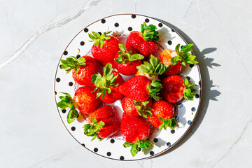 Fresh strawberries on polka dot plate over marble table - Top view with hard shadows.
