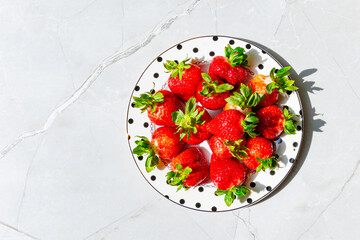 Fresh strawberries on polka dot plate over marble table - Top view with hard shadows.