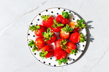 Fresh strawberries on polka dot plate over marble table - Top view with hard shadows.