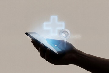 Hand holding smartphone with glowing holographic medical cross and stethoscope representing digital healthcare consultation