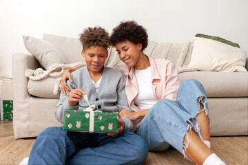 African American woman gives her son gift for Christmas, teenager celebrates New Year's with his mother and opens gift at home