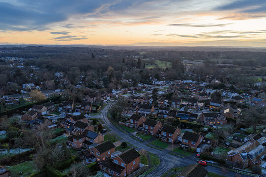 Aerial view of houses nestled amidst trees, a tapestry of warm terracotta roofs against the backdrop of a fading sunset, Hartley Wintney, England, United Kingdom.