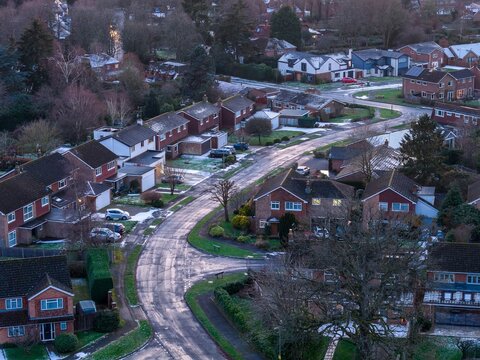 Aerial view of quiet streets lined with houses, the rooftops dusted with the remnants of winter's touch, Hartley Wintney, England, United Kingdom.