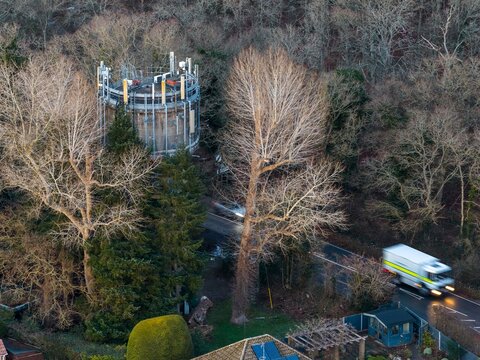 Aerial view of a cylindrical structure amidst the bare winter trees, with vehicles moving along the winding road, Hartley Wintney, England, United Kingdom.