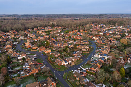 Aerial view of cozy homes nestled among bare trees and winding roads, where patches of snow hint at winter's touch, Hartley Wintney, England, United Kingdom.
