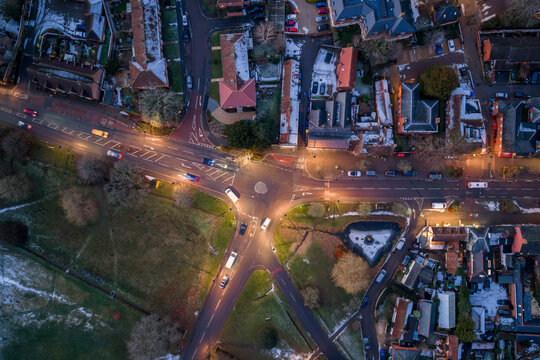 Aerial view of the roundabout with cars and snow-covered rooftops, lit by streetlights in the evening, Hartley Wintney, England, United Kingdom.