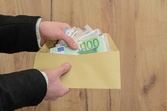Hands holding an envelope with a stack of euro banknotes in a business setting. Cash payment, corruption, financial transaction, bribery. Tax evasion, deal