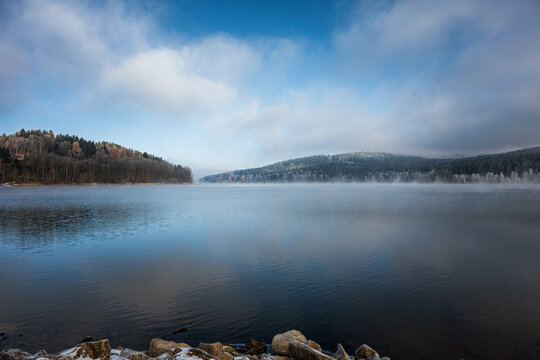 Frozen lake on the shores of Lake Lipno. Winter landscape with snowy trees, church with high tower. South Bohemia, Lipno