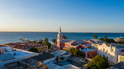 Aerial view of the vibrant red and white church steeple rising above historic buildings against the backdrop of the tranquil blue sea, Ilha de Mocambique, Nampula, Mozambique.